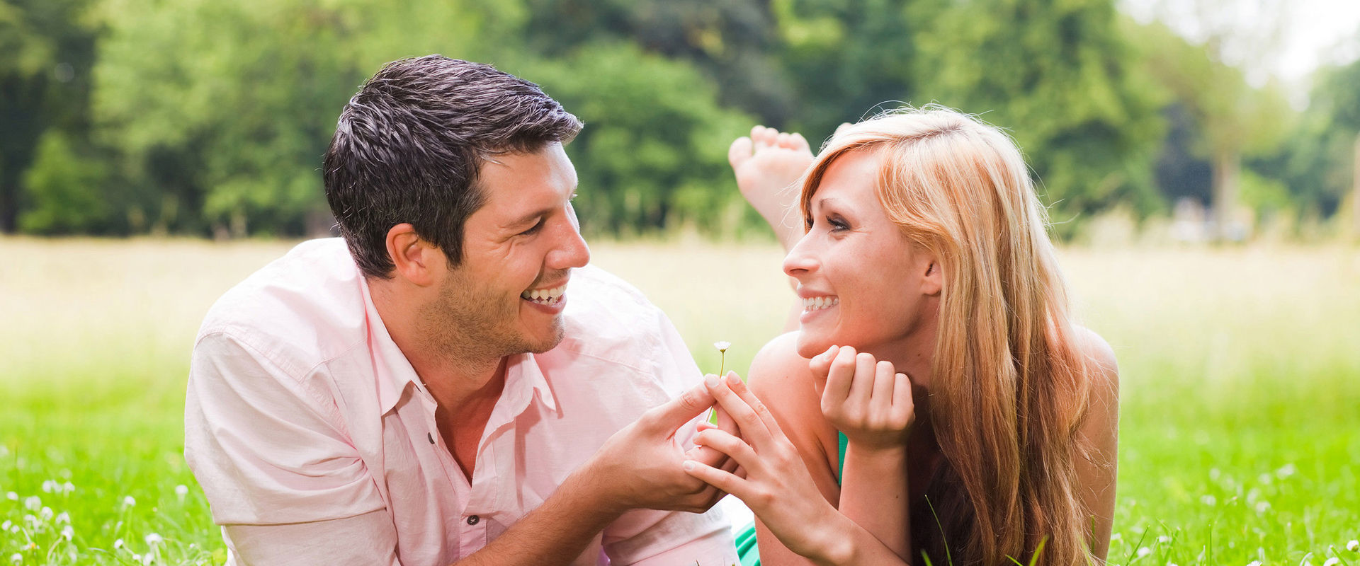 Couple in love on a meadow. A couple in love lie in a summer meadow. The man gives the woman a flower.